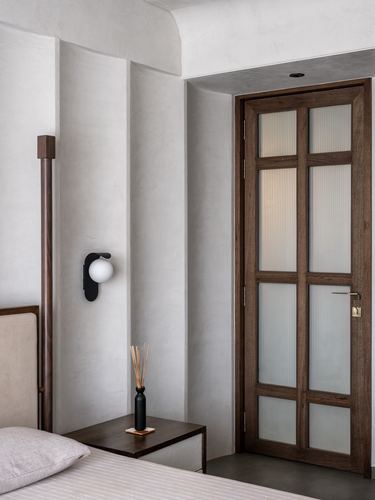 Bedroom corner with plaster wall, sconce, nightstand and fluted glass wood door