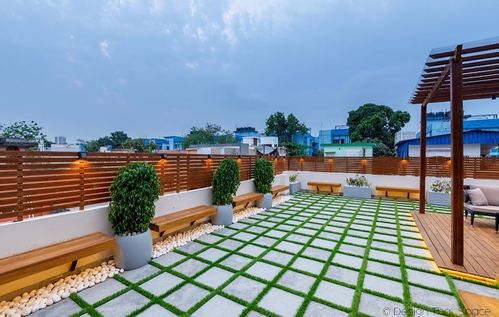 Rooftop terrace at dusk with grass-and-stone checkerboard flooring, wooden pergola, and potted plants