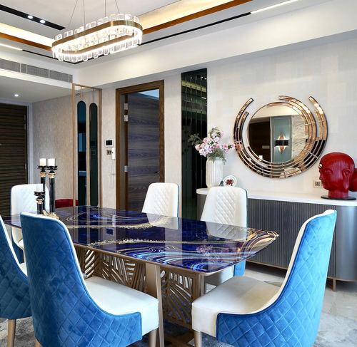 Dining room with blue-patterned table, velvet blue chairs, and round gold-framed mirror above sideboard