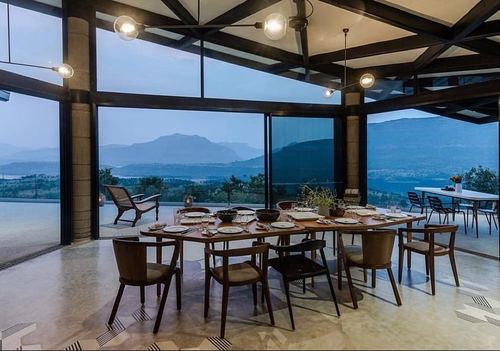 wooden dining table set inside glass-walled pavilion overlooking mountains at dusk