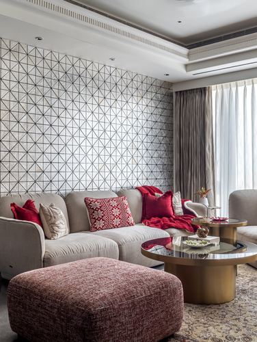 Living room with geometric stone feature wall, beige sectional sofa, red cushions and brass coffee tables