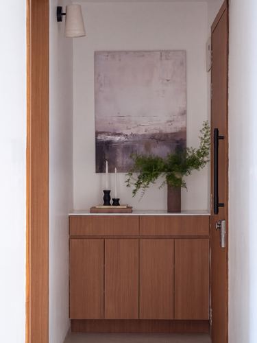 Wood-paneled foyer console with abstract painting, vase, and candle holders framed by open door