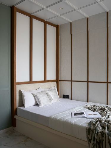 Minimalist bedroom with wood-framed panelled walls, upholstered headboard, and layered white bedding.