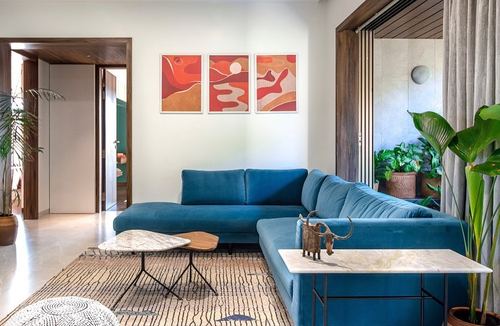 Teal velvet sectional sofa in a bright living room with marble side table and layered rugs