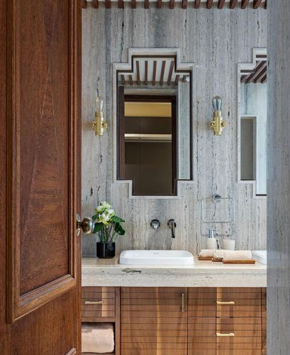 Bathroom vanity framed by open wood door, stone-clad wall with stepped mirror niche and brass sconces