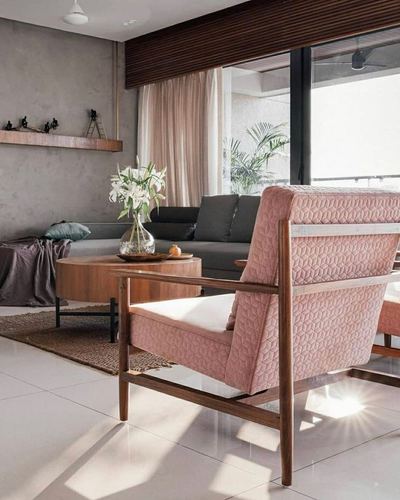 Blush quilted armchair with wooden frame in sunlit living room with grey sectional and glass balcony