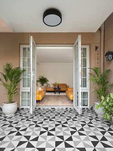 Entrance with black-white triangle tile floor, open french doors revealing orange sofa living room