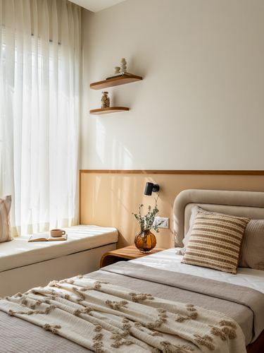 Sunlit bedroom corner with window seat, floating shelves, and upholstered bed with textured throw