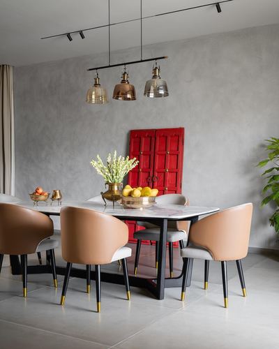 Dining table with tan leather chairs beneath cluster pendant lights, red antique door panel on grey wall