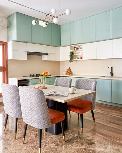 Sage green kitchen with white cabinetry beside a marble-top dining table with patterned chairs