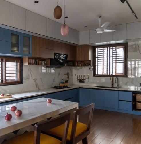 Blue and wood kitchen with marble-look backsplash, wooden windows, and mustard dining chairs