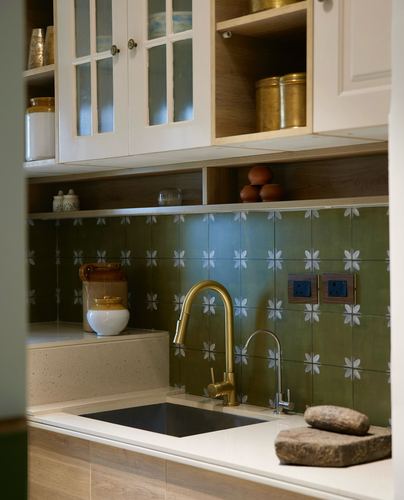 Kitchen corner with green floral-patterned tile backsplash, brass faucet, and white cabinetry