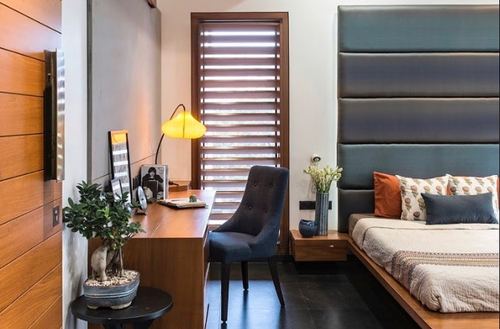 Bedroom with blue channel-tufted headboard, wooden desk nook, and louvered window with yellow lamp