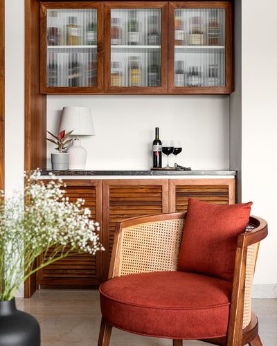 Cane-backed terracotta armchair before a wooden bar cabinet with reeded glass doors and wine set