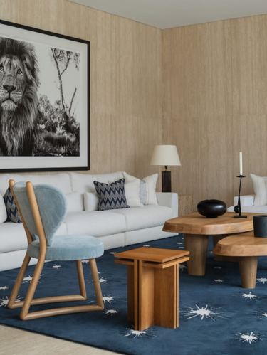 Living room with white sofa, blue velvet chair, wood coffee tables and navy star rug against travertine-clad wall