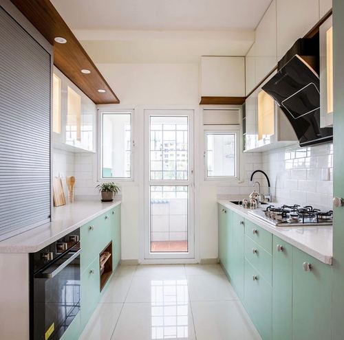 Parallel mint-green modular kitchen with white countertops and glass balcony door at the end