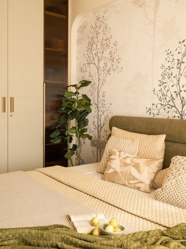 Bedroom corner with olive headboard, patterned wallpaper, arched wardrobe niche and a potted plant.