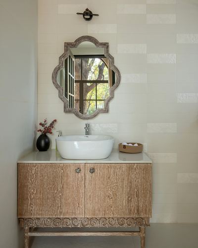 Bathroom vanity with carved wood cabinet, vessel sink, and scalloped mirror reflecting a window