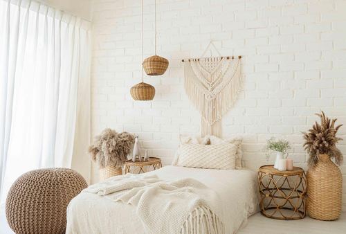 Boho bedroom with white brick wall, macrame hanging, rattan pendants, and a cream bed