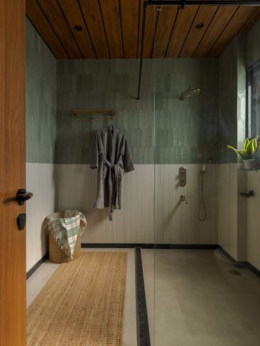 Open shower area with green tiled walls, wood-clad ceiling, hanging robe, and jute rug on entry floor