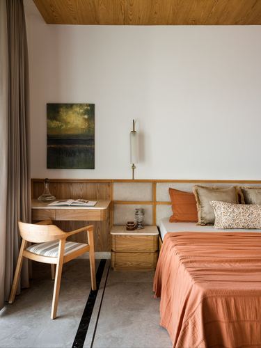 Bedroom with terracotta bedspread, wood-paneled headboard wall, and built-in study nook