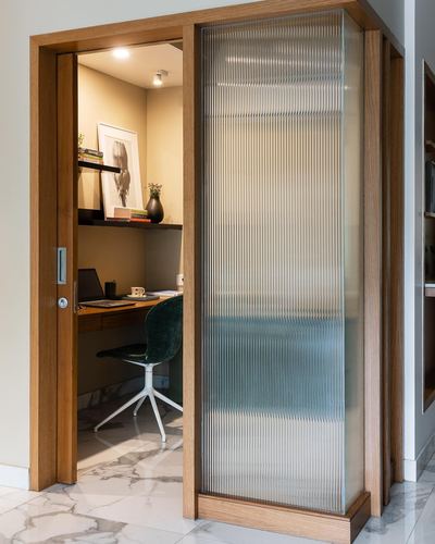 Study nook seen through open fluted glass door with desk, shelf and green chair