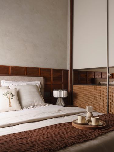 Bedroom corner with wood-panelled headboard, cane wardrobe, and tray of cups on a rust throw