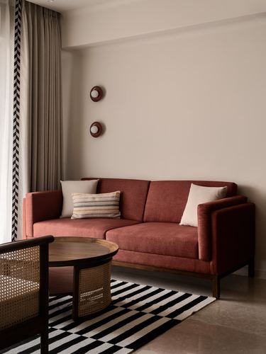 Terracotta sofa with cane armchair and round wood table on striped rug