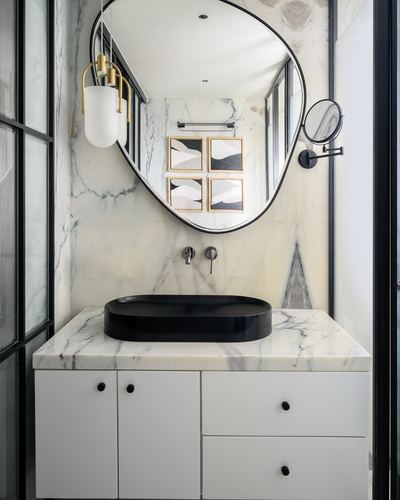 Marble bathroom vanity with black oval basin and irregular-shaped mirror above