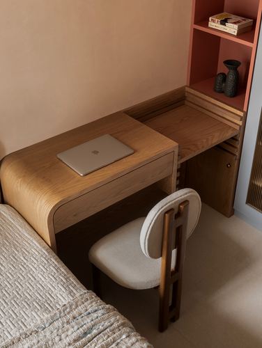 Curved wooden desk with laptop below a terracotta shelf, boucle chair, terrazzo floor