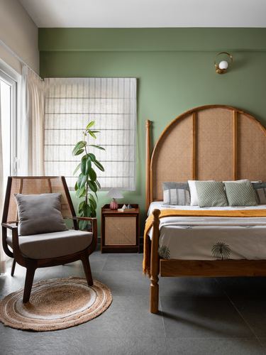 Green-walled bedroom with arched cane headboard bed and cane armchair by window