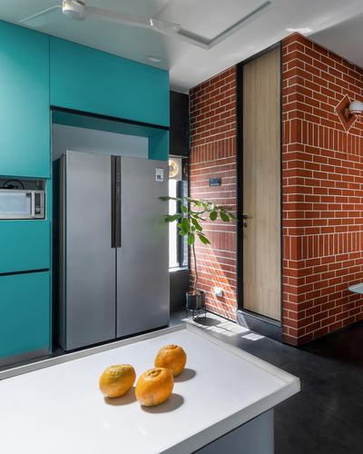 Teal kitchen cabinetry beside steel fridge and exposed brick wall with wooden door