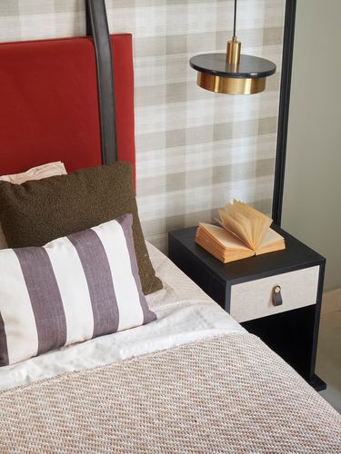 Red leather headboard beside black nightstand with open book under a brass pendant light