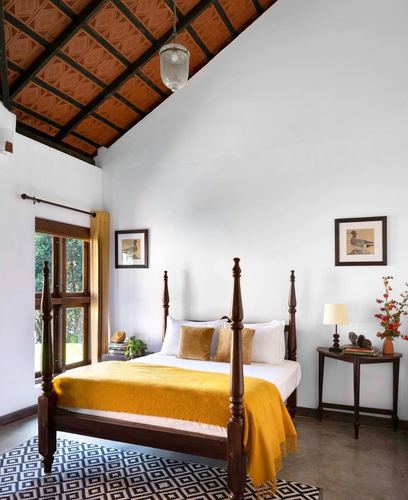 Kerala bedroom with carved four-poster bed, mustard throw, and exposed terracotta tile pitched ceiling