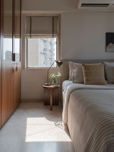 Sunlit bedroom corner with wooden wardrobe, upholstered bed and small wooden side table by window