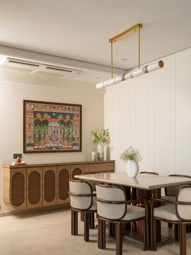 Dining area with floating wood sideboard, framed folk painting, marble-top table and curved chairs under a brass pendant