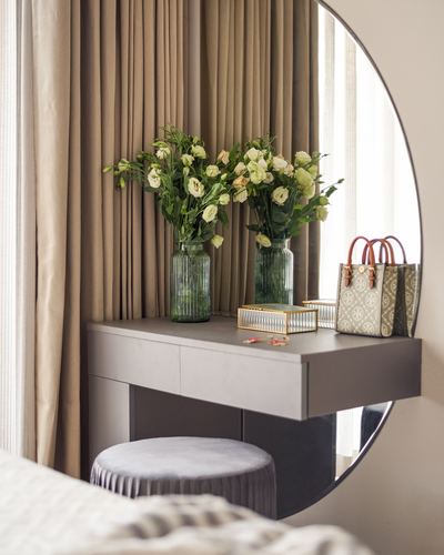 Floating vanity with flowers, mirror, and bag beside a velvet pouf