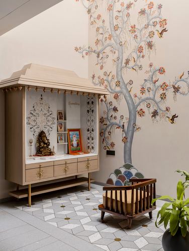 Wooden pooja cabinet with idols beside a painted tree mural and terrazzo floor