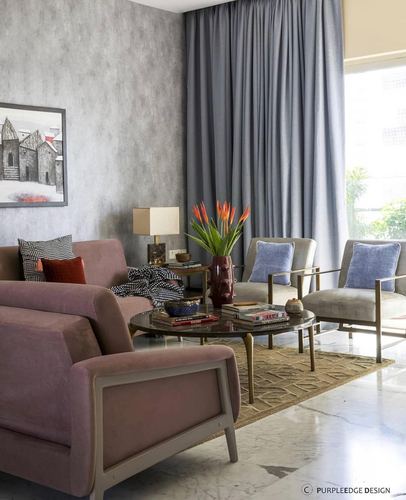 Living room with mauve velvet sofa, grey armchairs, brass coffee table and floor-to-ceiling curtains