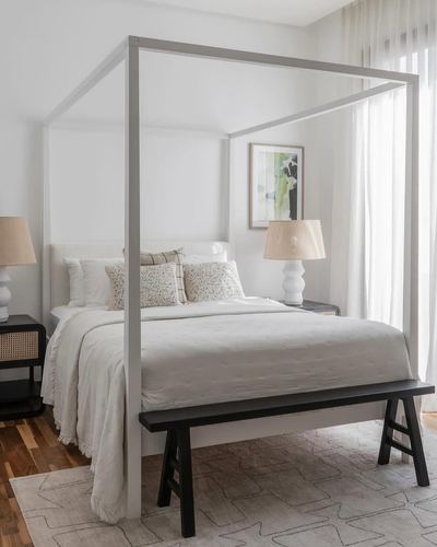 Minimalist bedroom with grey canopy bed, black bench, and cane nightstands
