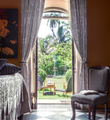 Arched door with floral curtains opens from a bedroom to a garden fountain, checkerboard floor in foreground