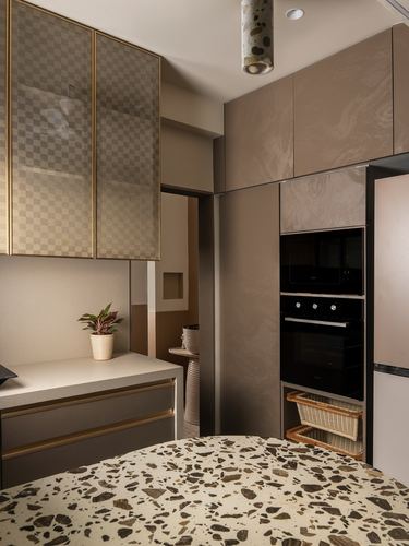 Taupe kitchen with checkered glass cabinets, terrazzo island, and built-in oven and microwave
