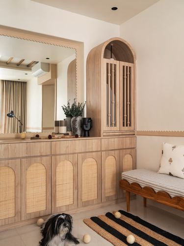 Wooden foyer cabinet with cane arches, arched mirror, bench and dog on striped rug