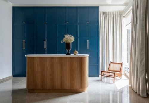 Bedroom with deep blue paneled wardrobes, fluted wood island, and cane lounge chair by window