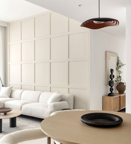 Minimalist living and dining room with paneled wall, white sofa, round wood table and sculptural pendant light