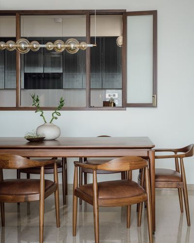 Wooden dining table with leather-cushioned chairs beneath a brass bubble pendant light and reeded glass cabinet.