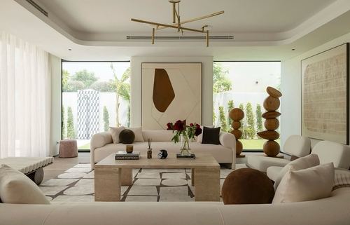 Cream sectional sofas around a stone coffee table beneath a brass chandelier, flanked by glass doors to a garden
