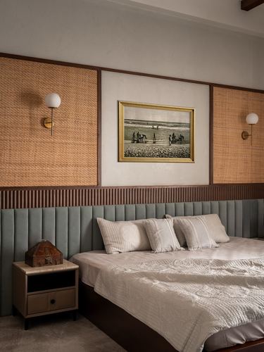 Bedroom with sage channel-tufted headboard, cane wall panels, brass sconces and framed seascape art