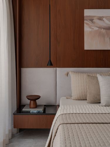 Bedroom corner with wood-panelled headboard wall, black pendant light, floating nightstand and beige bedding