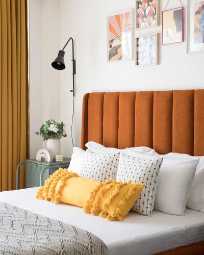 Bed with orange fluted headboard, yellow tasseled pillow, and colorful gallery wall above